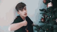 a young man in a black shirt is decorating a christmas tree with ornaments