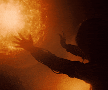 a person 's hand is reaching out towards a bright orange sun
