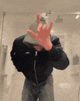 a man wearing a hat and a jacket is making a devil horns sign in front of a mirror .