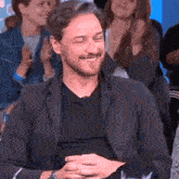 a man in a suit and black shirt is smiling in front of a crowd of people .