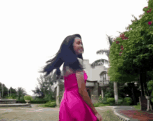 a woman in a pink dress is standing in front of a building