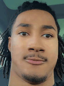 a young man with dreadlocks and a beard looks at the camera