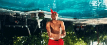 a shirtless man in red shorts and a red headband is standing in front of a swimming pool