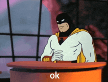 a cartoon character is sitting at a table and the word ok is on the table in front of him