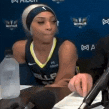 a female basketball player is sitting at a table with a microphone and a bottle of water .
