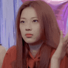a woman with red hair is wearing a red shirt and making a face .