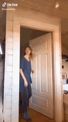 a woman in a blue shirt is standing in a doorway with her hair blowing in the wind .