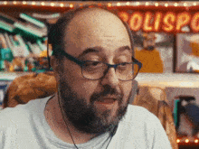 a man with glasses and a beard is sitting in front of a sign that says polisp