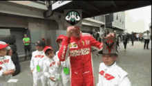 a man in a red and white lenovo racing suit holds a card over his face