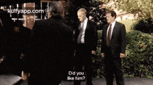 a group of men in suits and ties are standing next to each other and one of them is asking the other if he likes him .