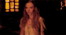 a woman in a white dress stands in a dark room with a candle in her hand