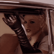 a woman wearing a veil and long black gloves is looking out of a car window