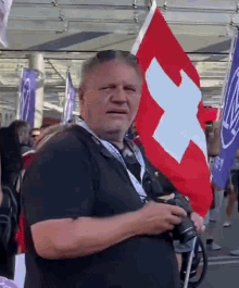 a man in a black shirt is holding a red and white swiss flag