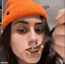 a woman wearing an orange beanie is eating a piece of food with a fork .