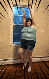 a woman in a blue tank top and shorts is dancing in a room
