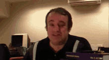 a man is making a funny face while sitting at a desk in front of a book titled microsoft history