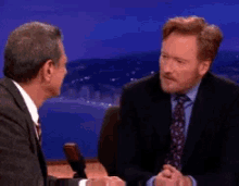 a man in a suit and tie is talking to another man on a television show