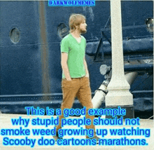 a man in a green shirt and brown pants is standing in front of a blue ship .