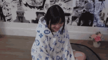 a woman is wrapped in a blue and white blanket and smiling while sitting on the floor .