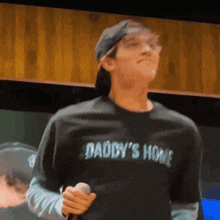 a man wearing a daddy 's home t-shirt is holding a microphone