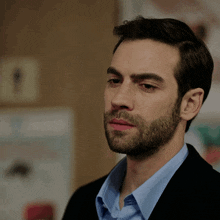a man with a beard wearing a blue shirt and black jacket