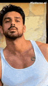 a man with a beard and mustache is wearing a white tank top and has a tattoo on his chest .