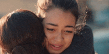 a woman is hugging another woman who is crying and looking at the camera .