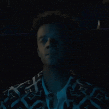 a man is sitting in a dark room wearing a louis vuitton jacket and a white shirt .