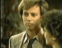 a man in a suit and tie is talking to a woman in a room .