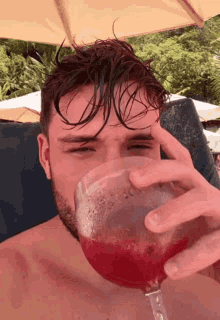 a shirtless man drinking from a wine glass