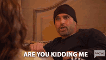 a man is sitting on a couch talking to a woman and the words are you kidding me are above him