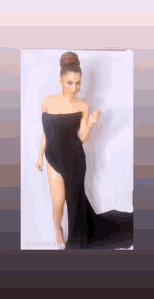 a woman in a black strapless dress is standing in front of a white wall .