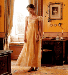 a woman in a yellow dress is standing in front of a desk