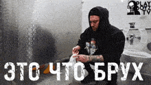 a man in a black hoodie sits in a public restroom with a play boyz logo
