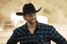 a man wearing a cowboy hat and plaid shirt is smiling