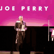 a man stands on a stage in front of a joe perry sign