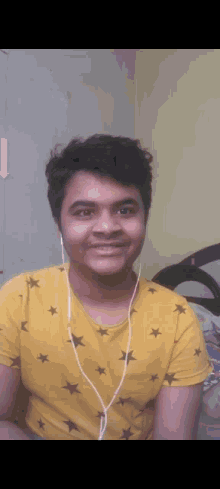 a young man wearing headphones and a yellow shirt with stars on it smiles for the camera .