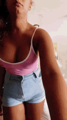 a woman in a pink top and blue shorts is taking a selfie