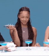 a woman sitting at a table holding a glass of blue liquid in her hand .