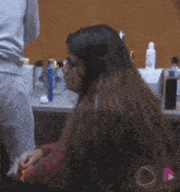 a woman with long hair is sitting in front of a counter with bottles of lotion on it