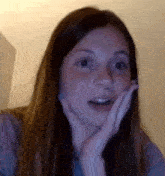 a woman with long hair is making a surprised face with her hand on her face .