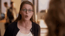 a woman wearing glasses and a black cardigan looks surprised