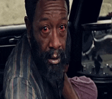 a man with a beard and red eyes is holding a baby in his arms .