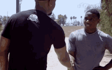 two men are standing next to each other and one is wearing a black t-shirt with a tennis ball on it