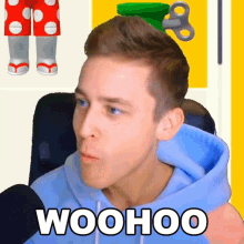 a man in a blue hoodie is sitting in front of a microphone and talking into it .