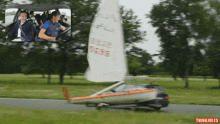 a car with a sailboat attached to it is driving down a road with trees in the background