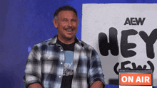 a man is smiling in front of a sign that says aew hey