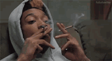 a man in a hoodie is smoking a cigarette with the words fullofsmoke behind him