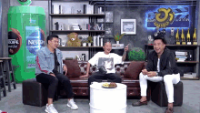 three men are sitting on a couch in front of a nescafe sign