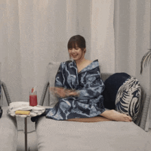 a woman in a robe is sitting on a couch with a drink in her hand